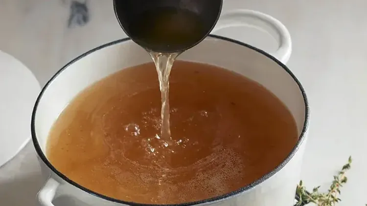 Concha despejando caldo de ossos dourado em uma panela branca